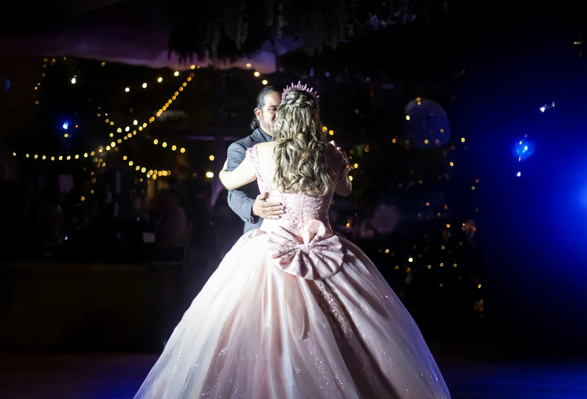 Bride and groom during the first dance in a darkened hall, warm string lights and bokeh behind them.