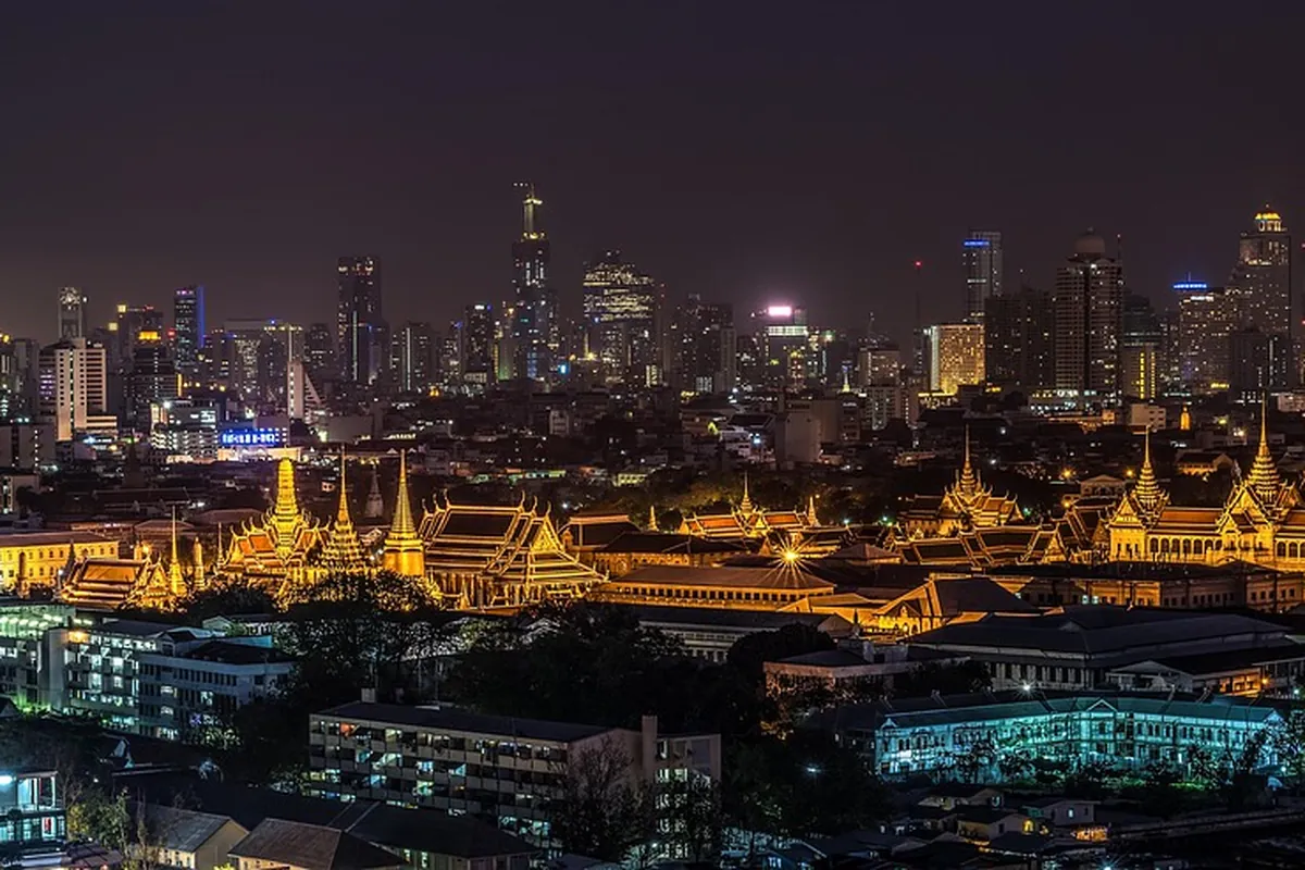 Bangkok skyline at night with an illuminated temple in the foreground and glass towers behind.