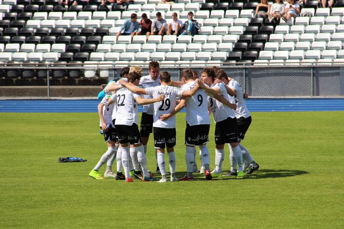 Amateur football team in white huddling and celebrating on the pitch.