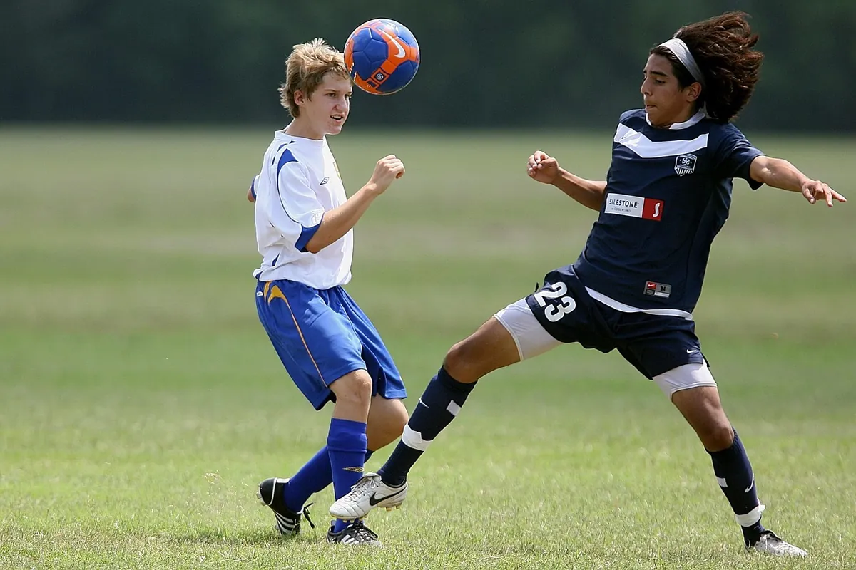 Two amateur footballers challenging for the ball on a green pitch.